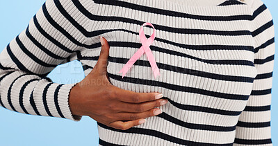 Hand, show pink ribbon and breast cancer support with awareness and health icon on blue background. Person in studio, medical symbol and wellness with care, trust and kindness in solidarity campaign