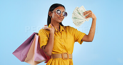 Woman, shopping bag and money fan, wealth and commerce with customer in sunglasses on blue background. Cash, financial freedom and retail, fashion and product choice, rich and shop discount in studio