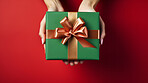 Hand holding a green gift box with gold bow, on a red table. Valentine, Christmas or birthday