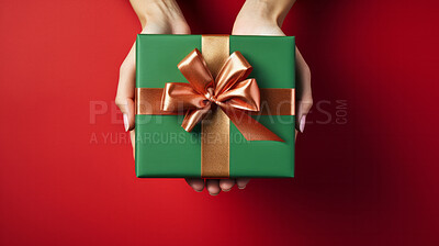 Hand holding a green gift box with gold bow, on a red table. Valentine, Christmas or birthday