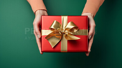 Hand holding a red gift box with gold bow, on a green table. Valentine, Christmas or birthday