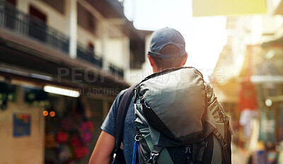 Buy stock photo Rearview shot of a young tourist wearing a backpack walking down a city street
