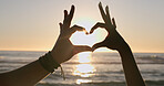 Love, hands and heart on beach with sunset, water background and horizon for vacation, travel or adventure. People, man and woman by ocean or sea with emoji for romance, care and relationship on trip