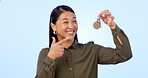 Smile, woman and pointing at keys for real estate, new home and property in studio isolated on a blue background mockup space. Happy person with keychain for house mortgage, apartment rent and moving