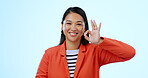Perfect sign, portrait and business woman in a studio for approval and satisfaction hand gesture. Happy, smile and professional young Asian creative designer with ok emoji isolated by blue background