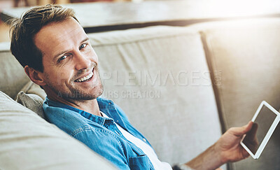 Buy stock photo High angle portrait of a man using his tablet while sitting on the sofa at home