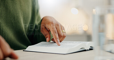Closeup hand, reading and a bible for faith, spiritual support or hope from scripture. House, table and a person with a book for worship, trust or education on God, Jesus or learning about religion
