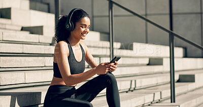 Runner woman, headphones and phone on stairs with music, smile and relax in city, workout and training. Girl, smartphone and happy with audio streaming subscription with typing, social media or app