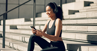 Runner girl, headphones and phone on stairs with music, smile and relax in city, workout and training. Woman, smartphone and sitting with audio streaming subscription with typing, social media or app