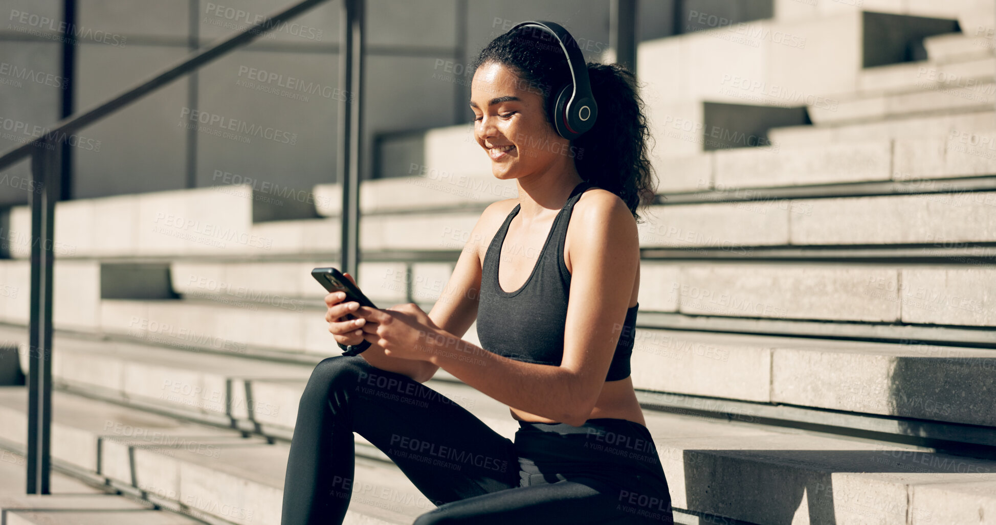 Buy stock photo Runner girl, headphones and phone on stairs with music, smile and relax in city, workout and training. Woman, smartphone and sitting with audio streaming subscription with typing, social media or app
