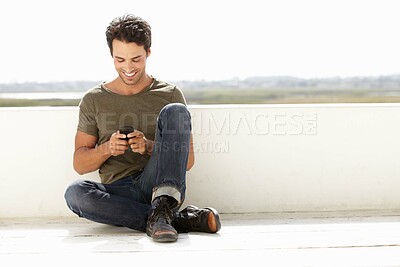Buy stock photo A handsome young man sending a text message while sitting outside