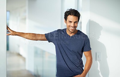 Buy stock photo Portrait of a handsome young man standing in a passageway and smiling while leaning with one hand against a wall and the other in his pocket
