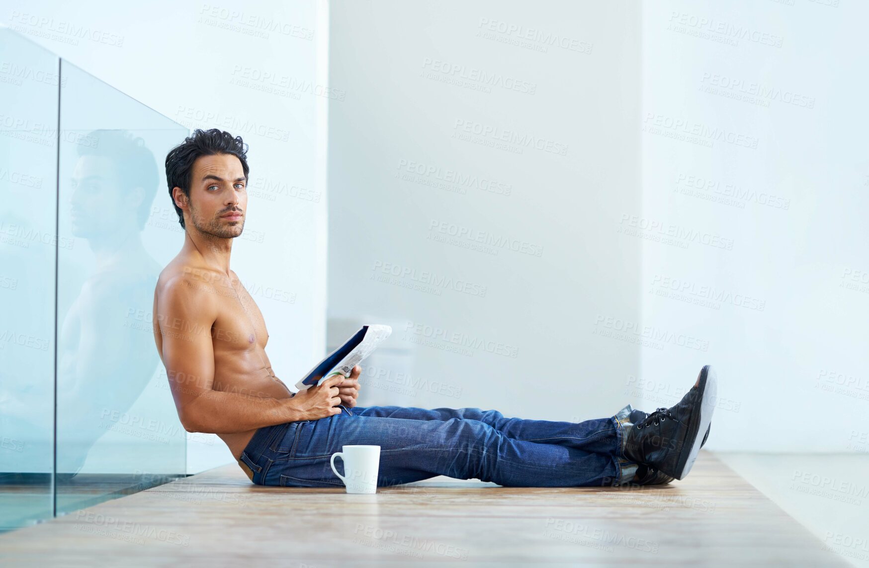 Buy stock photo Portrait of a handsome young man with a tattoo sitting on the floor having a cup of coffee and reading a newspaper