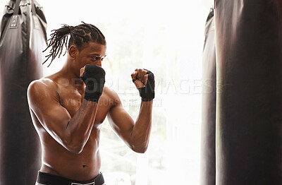 Buy stock photo Shot of a young boxer practicing on a punching bag in a gym