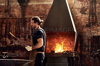 Buy stock photo Cropped shot of a handsome young metal worker sharpening a hot metal rod inside a welding workshop