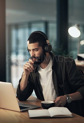 Buy stock photo Shot of a young businessman using a laptop and headphones during a late night at work