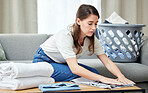 Laundry, woman and fold clothes in living room of home with housekeeping, spring cleaning and housework. Person, cleaner and packing washing on sofa in lounge with basket, serious and domestic work