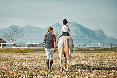 Woman leading child on horse, ranch and mountain in background lady and animal walking on field from back. Countryside lifestyle, rural nature and farm animals, mom teaching kid to ride pony in USA.