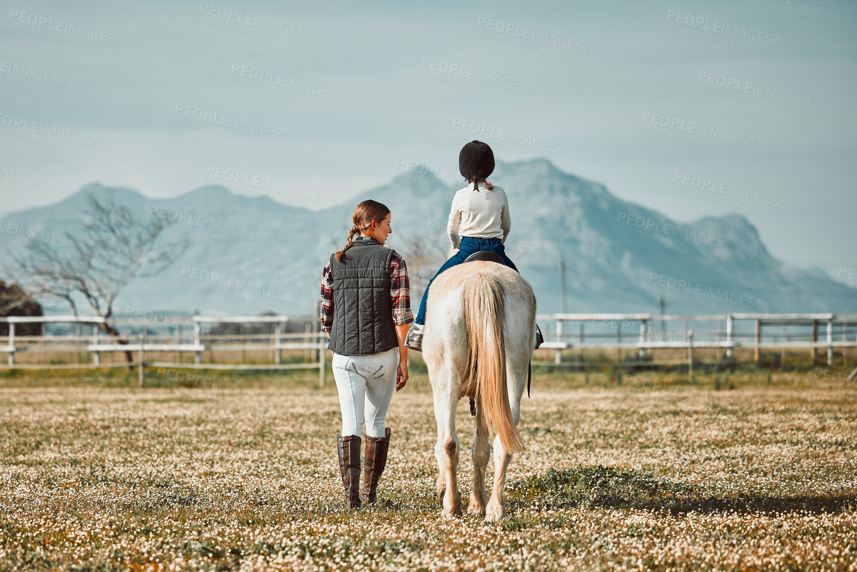 Buy stock photo Woman leading child on horse, ranch and mountain in background lady and animal walking on field from back. Countryside lifestyle, rural nature and farm animals, mom teaching kid to ride pony in USA.