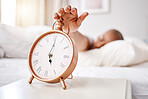 Hand, alarm and person wake up in bed in the morning after rest and relax at home. Bedroom, clock and sleeping or tired at sunrise with a watch or timer with a closeup for snooze on a table