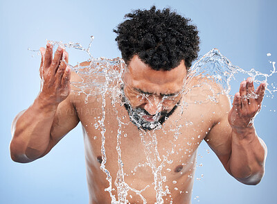 Buy stock photo Black man, water splash and face wash for skincare, hygiene or grooming against a blue studio background. African male person, model and aqua for body hydration, shower or facial skin treatment