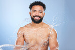 Black man, portrait and water splash for skincare, hygiene or grooming against a blue studio background. Face of African male person, model and smile for body hydration, shower or aqua for soft skin