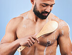 Man, shower and brush for cleaning in studio with armpit, scrub and thinking for hygiene by blue background. Person, guy and foam for spa, cosmetics and wellness for body, skincare and healthy