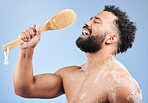 Shower, singing and man with brush in studio for cleaning, wellness or morning routine on blue background. Bathroom, karaoke and male model having fun with body scrubber, cosmetics or luxury washing