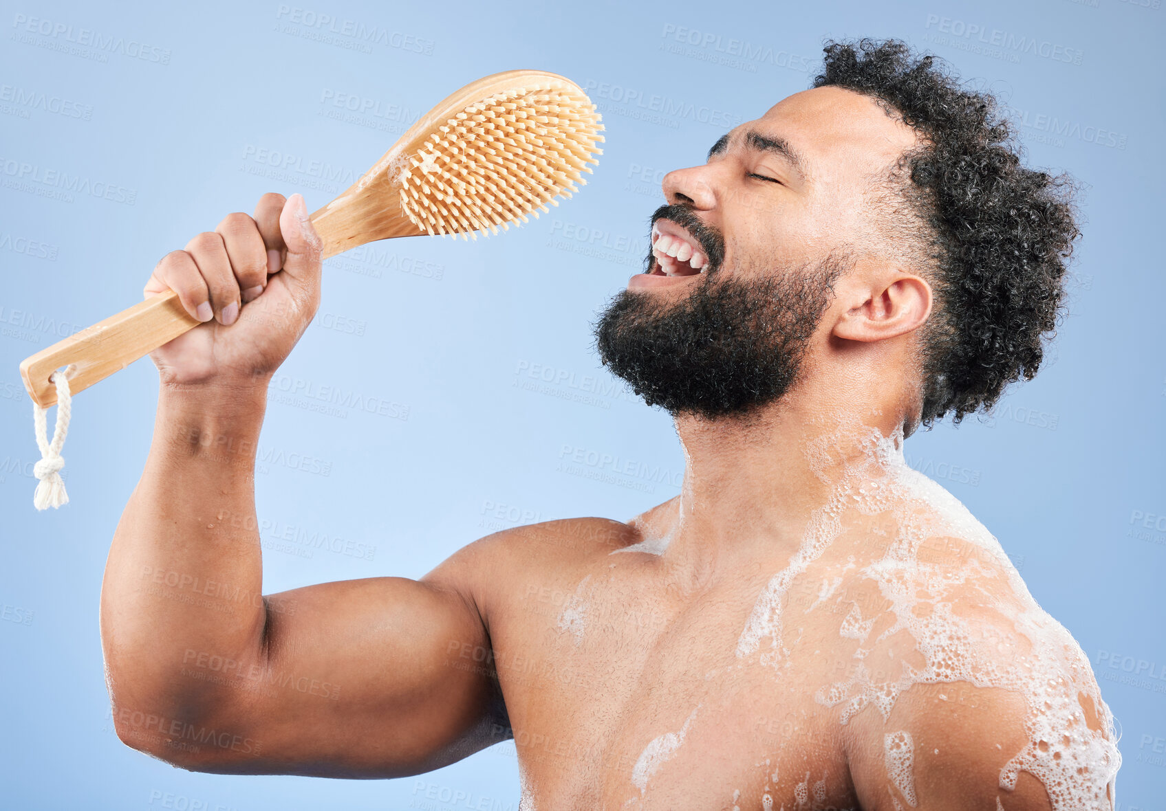 Buy stock photo Shower, singing and man with brush in studio for cleaning, wellness or morning routine on blue background. Bathroom, karaoke and male model having fun with body scrubber, cosmetics or luxury washing