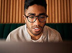 Young man, nerd and glasses reading on laptop in cafe for remote work, research or online connection. Closeup of smart person, face or focus on computer for search, email or freelancer at coffee shop