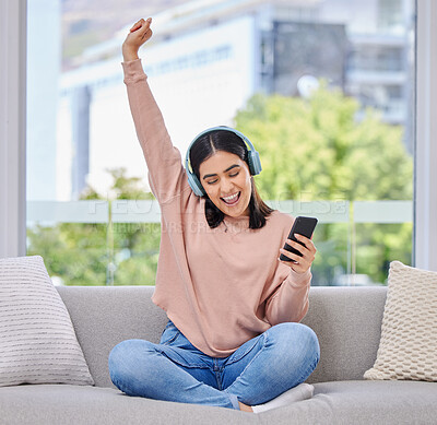 Buy stock photo Woman, excited and phone with headphones for music on a home sofa with happiness and energy. Happy female person on a lounge couch with a smartphone for streaming or listen to audio, podcast or radio