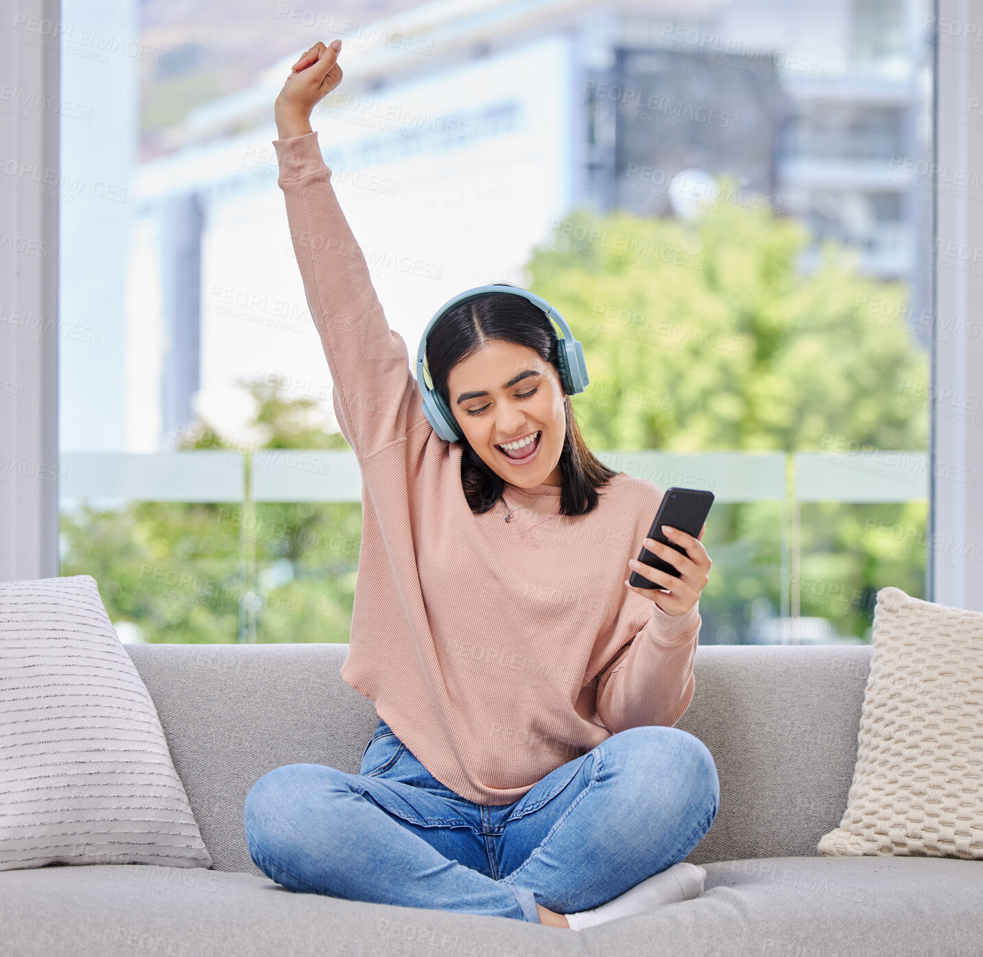 Buy stock photo Woman, excited and phone with headphones for music on a home sofa with happiness and energy. Happy female person on a lounge couch with a smartphone for streaming or listen to audio, podcast or radio