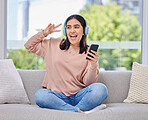 Woman, headphones and smartphone for singing on sofa for happiness, relax and music in home living room. Girl, phone and audio streaming subscription for hip hop, rock or edm with peace sign in house