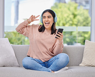 Buy stock photo Woman, headphones and smartphone for singing on sofa for happiness, relax and music in home living room. Girl, phone and audio streaming subscription for hip hop, rock or edm with peace sign in house