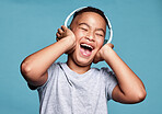 Children, headphones and music with a funny boy streaming audio in studio on a blue background. Kids, radio and listening with a little, young male child enjoying a popular track on the internet