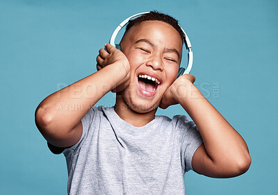 Buy stock photo Children, headphones and music with a funny boy streaming audio in studio on a blue background. Kids, radio and listening with a little, young male child enjoying a popular track on the internet