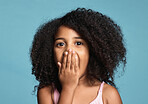 Black child, surprised and shocked with wow expression covering mouth in awe feeling positive and excited with natural afro hair. Face portrait of cute kid amazed and happy against blue background