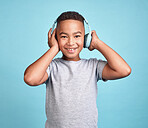 Children, music and headphones with a boy listening to the radio or streaming audio in a studio on a blue background. Kids, online and track with a young male child enjoying a song with technology