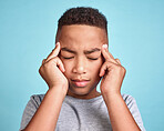 Child with headache, stress and mental health problem or fatigue pain on blue studio background. Frustrated african american kid, depressed boy and angry youth with fingers massaging temples of head