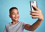 Phone, selfie and boy child with happy smile for confident and carefree digital photograph fun. Cheerful male preteen smiling for smartphone camera picture with blue background for mock up.