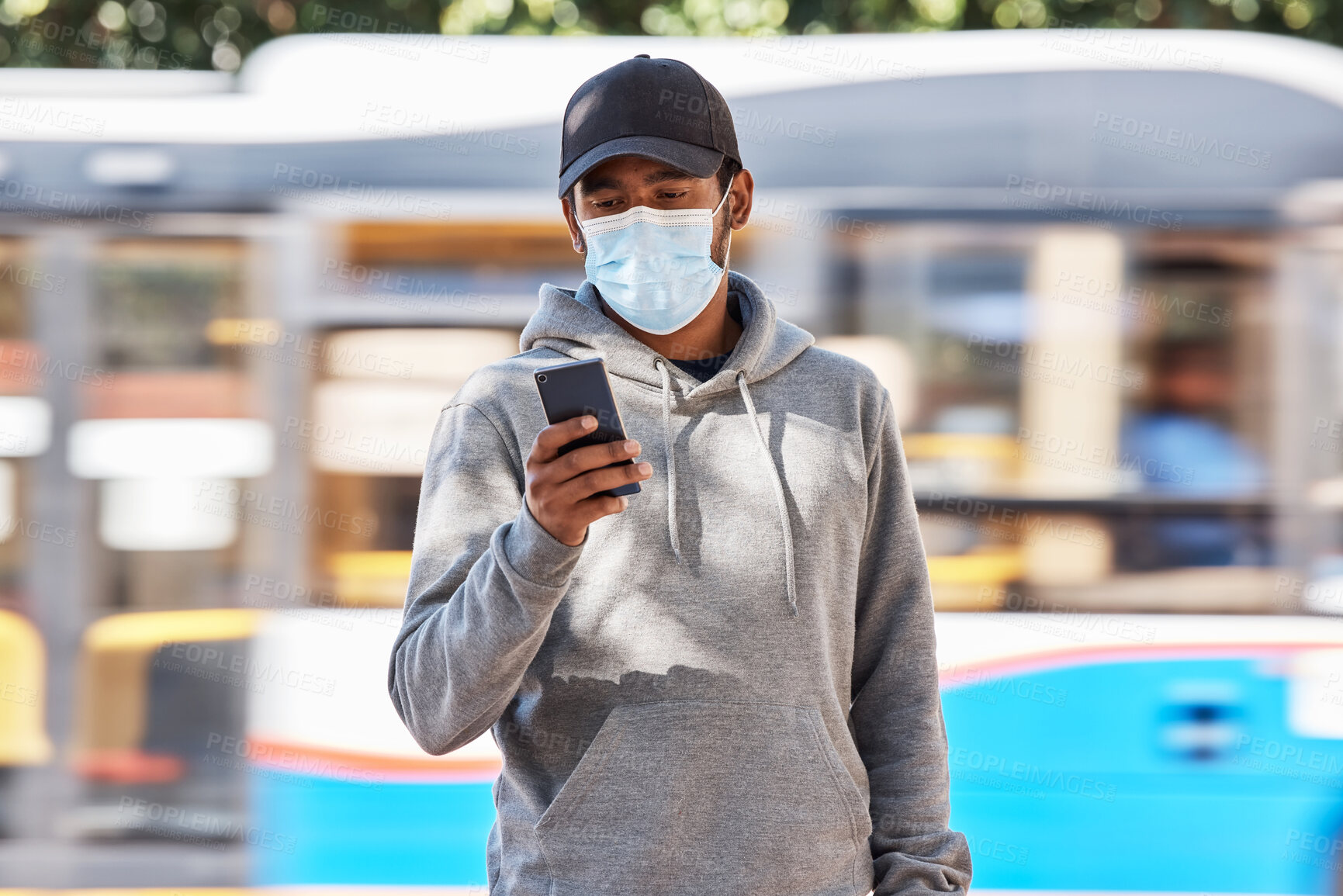 Buy stock photo Man in city with mask, phone and travel in morning at bus stop, checking service schedule or social media. Public transport safety in covid, urban commute and person in street with smartphone app.