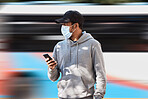 Man in city with mask, phone and bus stop for morning travel, checking service schedule or location. Public transport safety in covid, urban commute and person in street with smartphone on mobile app