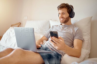 Buy stock photo 5g internet, video and online streaming of a man on a computer and phone in bed. Happy guy with a smile relax and multitask listening to a digital radio podcast or web music with modern technology 