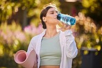 Fitness, woman and water for hydration in yoga for healthy, exercise or workout in the nature outdoors. Female drinking from bottle holding mat for exercising, training and wellness in health sport