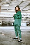 Portrait, fashion and stylish young gen z woman standing in a warehouse while wearing green clothing. Trendy, hipster latino girl with curly hair in industrial building or factory with pride or cool
