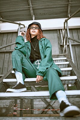 Buy stock photo Woman, street fashion and model in city for trendy gen z portrait. Freedom, urban lifestyle and young black girl with stylish hip hop clothes, sunglasses and hat on building stairs in urban town