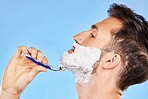 Shave, cream and man grooming his beard with a shaver in studio for health, skincare and hygiene. Foam, razor and model shaving his facial hair for a face or skin routine isolated by blue background.