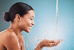 Skincare, health and black woman with water splash, wellness and hygiene against a blue studio background. Cosmetics, young female and girl with smile, drops and natural beauty for washing and relax.