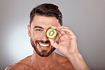 Man, face and beauty with kiwi, facial care with wellness and organic treatment against studio background. Natural skincare, fruit and eye, wellness mockup with cosmetic care and smile in portrait