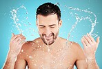 Water, skincare and man with facial splash, smile and morning cleaning treatment isolated on blue background. Face, hygiene and male model grooming for health, wellness and clean skin care in studio.